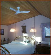 Large Master Bedroom (showing Queen-sized brass bed, not included), has cathredral pine ceilings, two windows, hardwood floors, ceiling fan, double closet, neutral tones.
